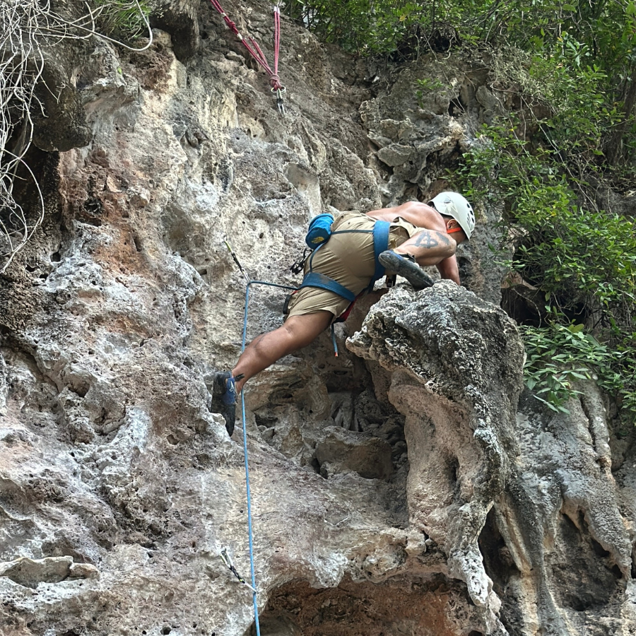 Climber sitting atop a rock ledge on Ling Noi, Railay Beach, enjoying a scenic monkey-like perch after a successful ascent.